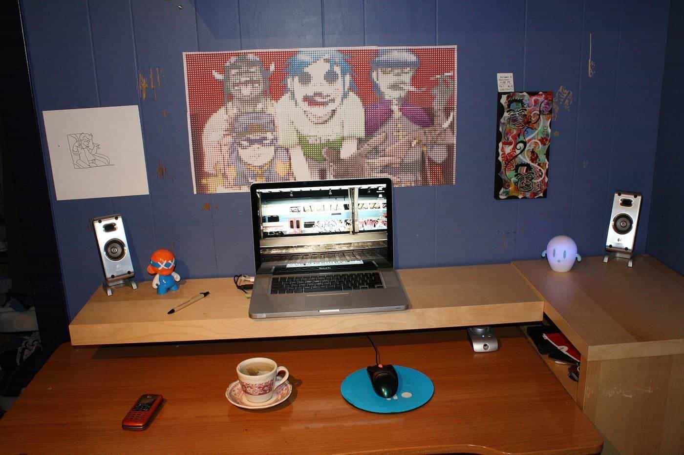 A home office desk with a laptop, speakers and artwork on the wall