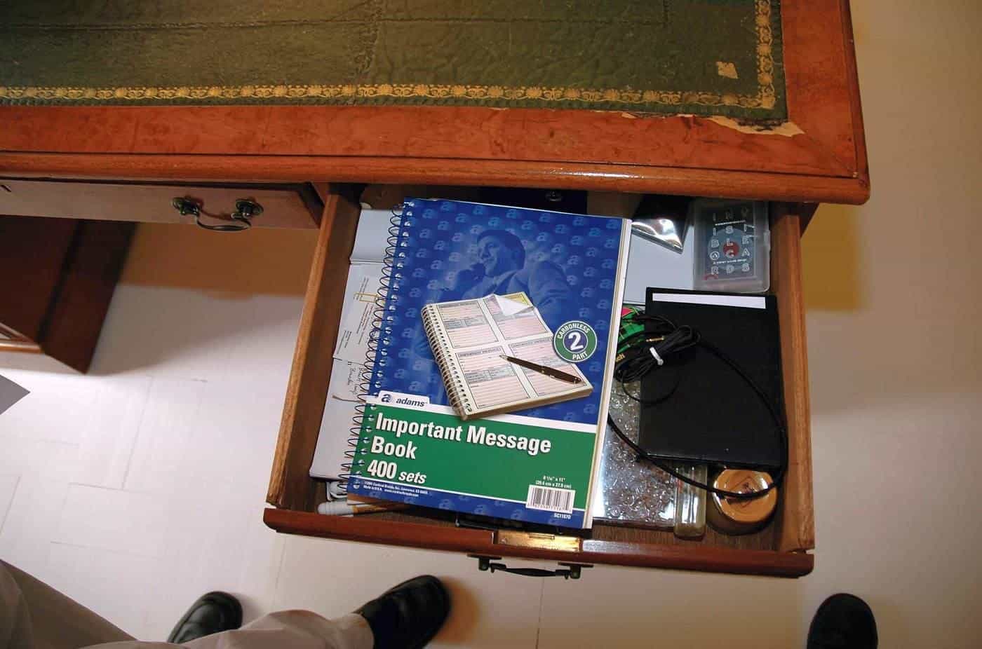 An open wooden desk drawer with notebooks and stationery