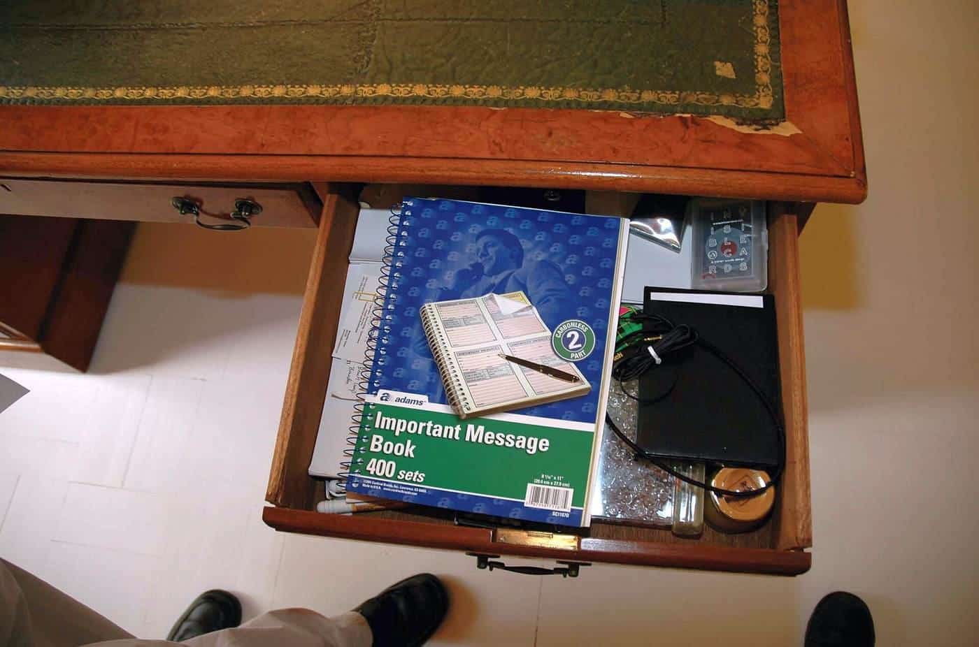 An open wooden desk drawer with notebooks and stationery