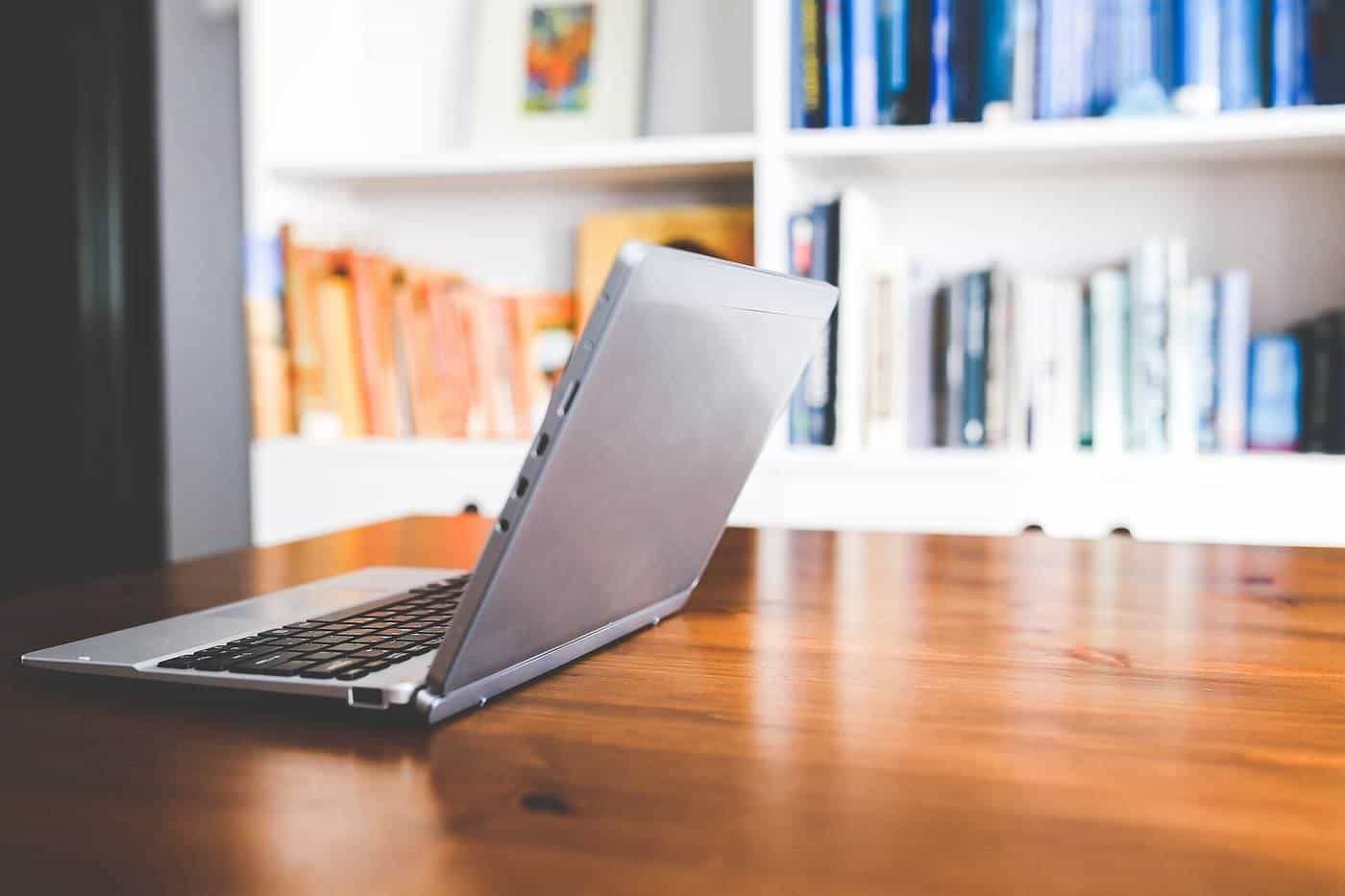A laptop on a wooden desk in front of bookshelves