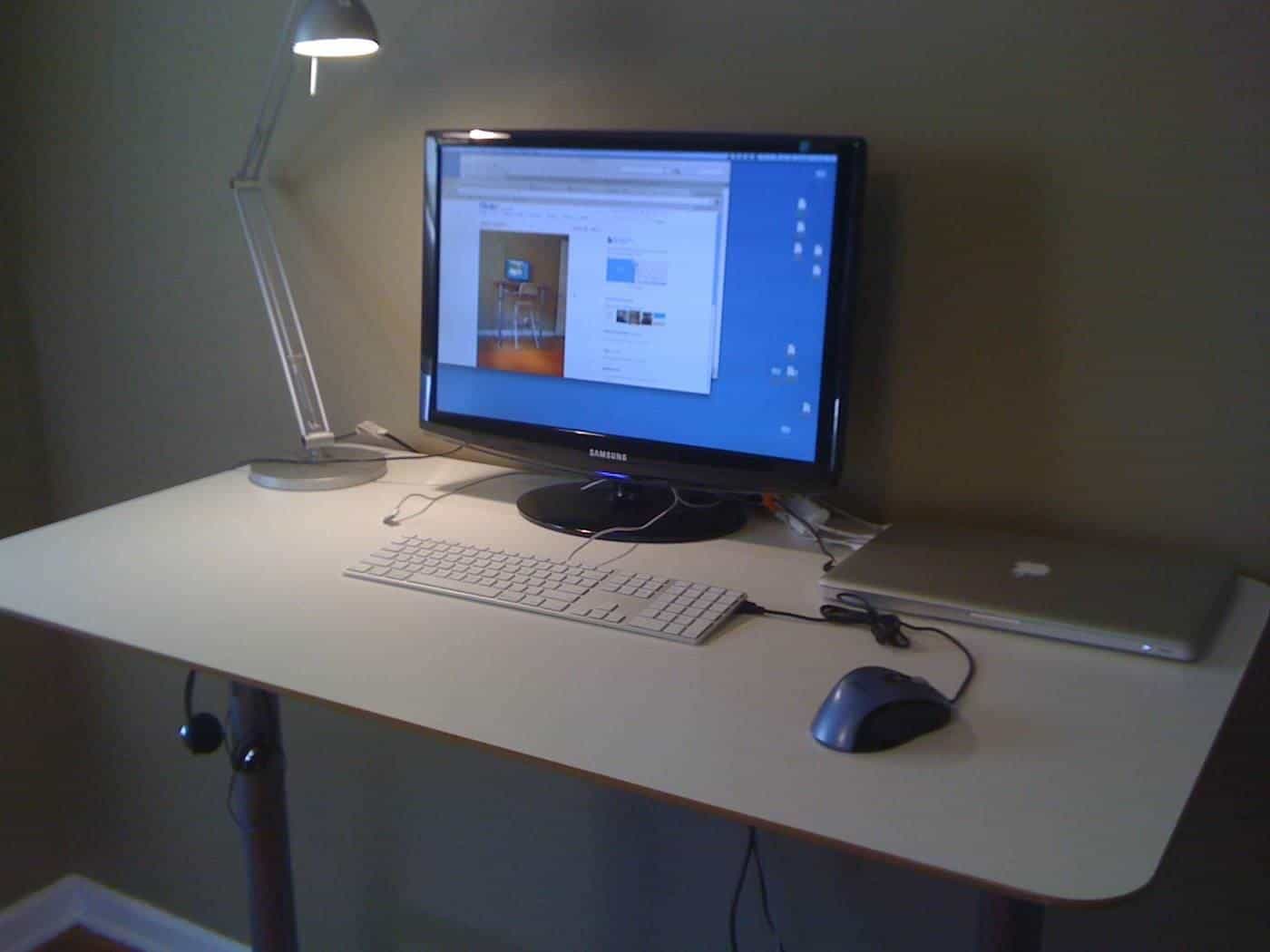 A standing desk with a monitor, keyboard and lamp in an office