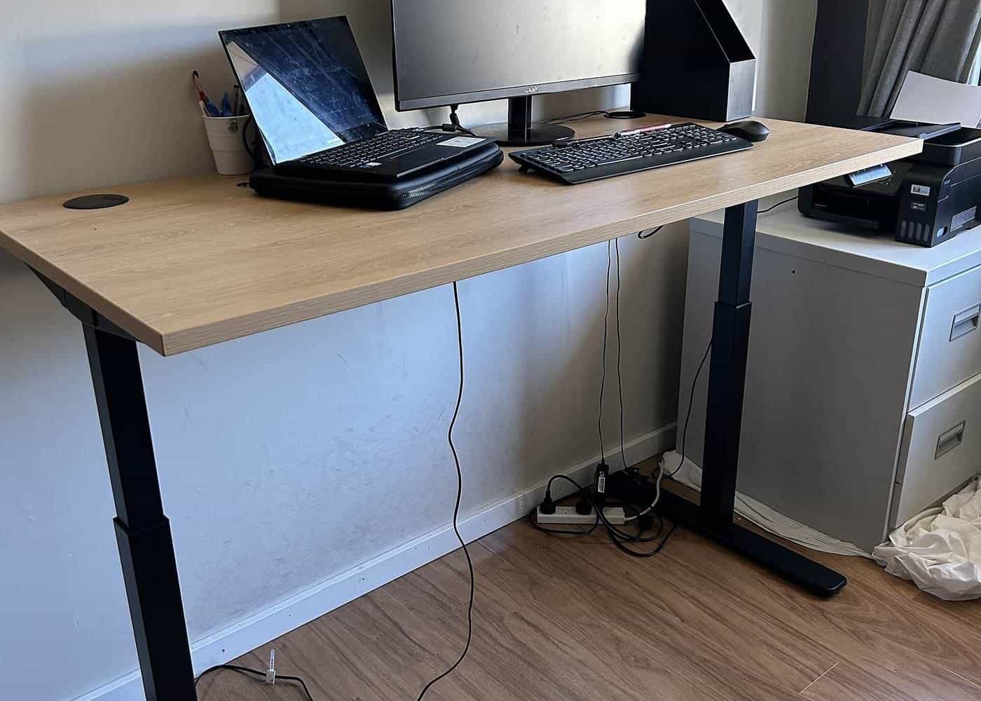 A height-adjustable desk with a laptop and monitor in an office