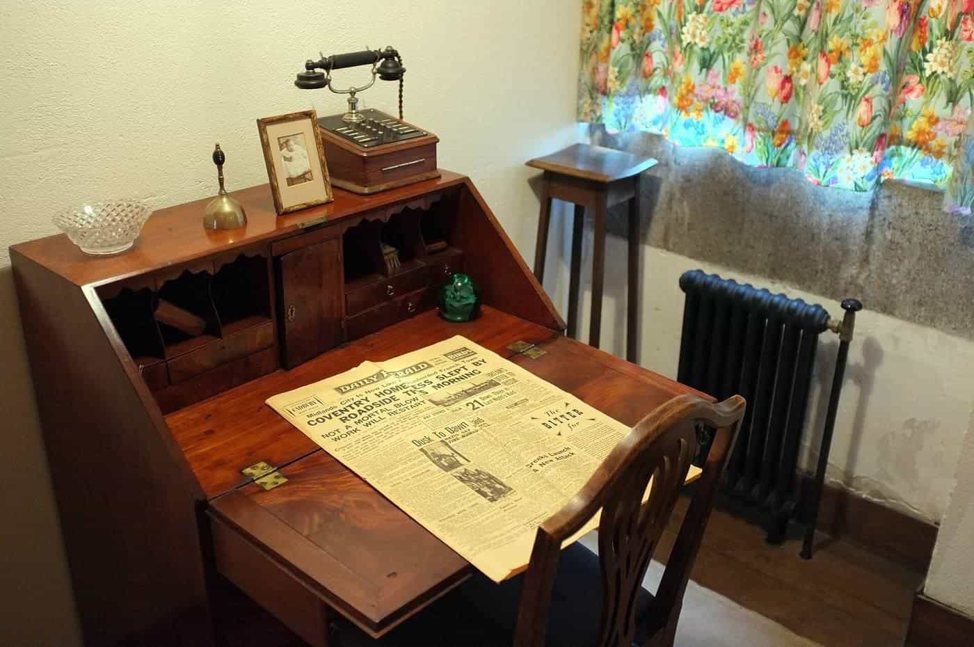 A wooden writing desk with papers and a lamp