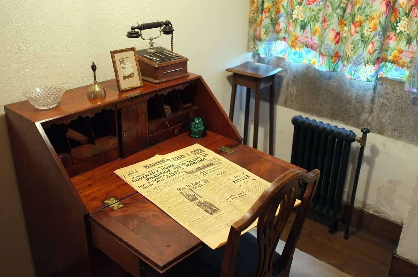 A wooden writing desk with papers and a lamp